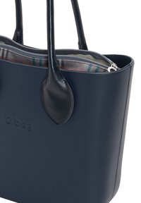 Granatowa torba typu tote O bag o gładkiej powierzchni. Posiada skórzane uchwyty, zamek błyskawiczny oraz podszewkę z wzorzystej tkaniny w odcieniach szaro-niebieskich.