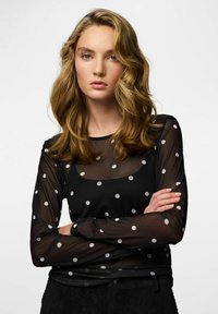 Czarna, prześwitująca bluzka z długim rękawem w białe kropki. Okrągły dekolt i dopasowany krój. Miękki, lekki materiał z lekką przezroczystością.