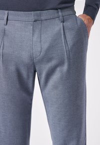 Pantaloni grigi su misura realizzati in un tessuto liscio, con vita piatta, doppie pieghe e tasche laterali, per un aspetto strutturato.