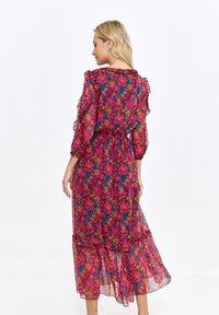 Floral maxi dress in sheer fabric, featuring vibrant pink, orange, and blue flowers. Ruffled sleeves and tiered hem add texture and detail.