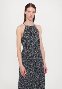 Halter neck -mekko mustalla taustalla, jossa on pieniä sinisiä kukkakuoseja. Vyötärö on korostettu hopeaketjulla.