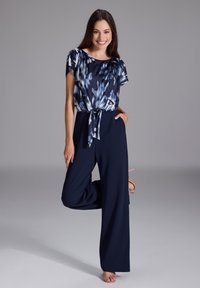 Combinaison marine à jambes larges, avec un haut à manches courtes à motif floral et un détail de taille nouée. Tissu lisse avec une légère brillance.