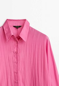Roze overhemd met knoppen en een gestructureerde kraag, met een gladde, iets gekreukte textuur en zeven bijpassende knopen aan de voorkant.