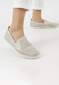 Lichtgekleurde instapschoenen met een geperforeerd ontwerp, voorzien van zwarte stippen, rubberen zolen en een gladde textuur. Geaccentueerd met een subtiele beige voering.