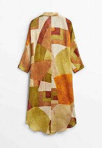 Veste-chemise longue en tissu léger présentant un motif géométrique dans des tons terreux de vert, marron et crème. Manches courtes, col.