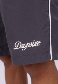 Mørkegrå shorts fremstillet af letvægtsstof, med hvidt kantbånd og broderet "Dropsize" logo ved kanten.