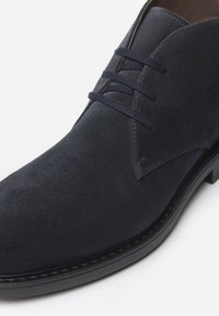 Stivale alla caviglia in suede blu navy con finitura liscia, chiusura con lacci a quattro fori e punta rotonda. Suola in gomma nera dettagliata con cuciture.