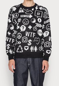 Maglione nero con motivi grafici bianchi, inclusi simboli ed emoji. Presenta un colletto e polsini a costine, con una vestibilità rilassata.