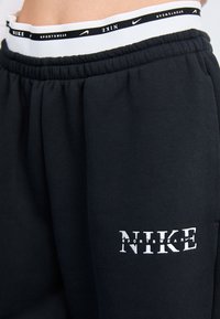 Pantalones de chándal negros hechos de una tela suave, que cuentan con una cinturilla elástica con marcas en negro y blanco y un logo de Nike blanco en el muslo.