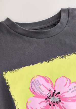 Maglietta di cotone grigia con scollo rotondo, con una grande grafica di un fiore rosa contornato di nero su uno sfondo giallo brillante.