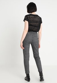 Černý krajkový top s krátkým rukávem s vzorem, doplněný šedými texturovanými kalhotami. Kalhoty mají slim fit a vysoký pas. Celkový vzhled doplňují černé kotníkové boty.