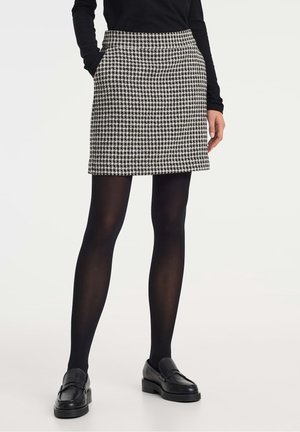 Jupe pied-de-poule noir et blanc avec un design ajusté, des poches latérales et un ourlet droit, assortie à des collants noirs et des mocassins.