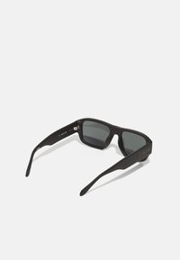 Gafas de sol negras con lentes oscuros, montura rectangular y textura suave. Presenta un sutil branding en los laterales y brazos robustos.