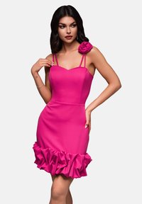Tätt sittande rosa klänning med spaghettiband, volangnert kant och en blommig accent på axeln, tillverkad av slät och stretchig tyg.