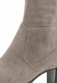 Gray suede ankle boot with a smooth texture, curved design, stitched accents, and a high heel. Close-up view showing material details.