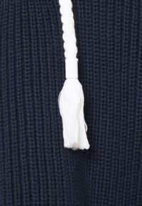 Tessuto lavorato a maglia blu navy con un cordino bianco intrecciato e punta in plastica. La consistenza è grossa con schemi di cucitura visibili.