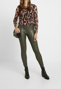 Tunn långärmad topp med ett rosa och brunt leopardmönster, ihop med figursydda olivgröna leggings och svarta ankelstövlar. Svart handväska ingår.