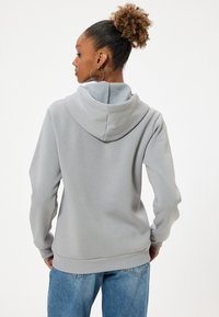 Sudadera gris claro con una textura suave, de mangas largas y una capucha grande. Presenta puños y dobladillo acanalados, combinada con unos jeans de mezclilla azul.