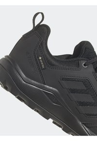 Scarpa sportiva nera con tomaia in sintetico testurizzato, caratterizzata da un'etichetta Gore-Tex, suola robusta e design a strati tridimensionale.