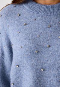 Helles, blaues Strickoberteil mit Rundhalsausschnitt, verziert mit verstreuten kleinen glitzernden Strasssteinen.