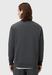 Sudadera gris con cuello redondo, mangas largas y puños acanalados. La tela parece suave con una textura lisa y un diseño de corte relajado.