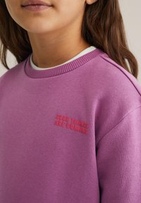 Vijolična sweatshirt s rebrastim izrezom, na sprednji strani pa se nahaja napis "DOBRE STVARI PRIHajajo" v dvignjenem rdečem vezenju. Mehak material.