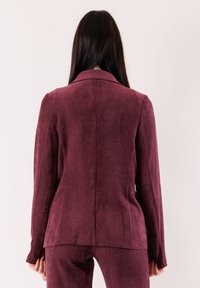 Blazer su misura color bordeaux con finitura strutturata, maniche lunghe e collo a revers con spacco posteriore, caratterizzato da una silhouette elegante e dettaglio con spacco sulla schiena.