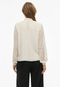 Lyscremet bluse med teksturerede polka dot gennemsigtige ærmer, en flæsekrave og elastiske manchetter. Enkel ryg med en nøglehul detalje.