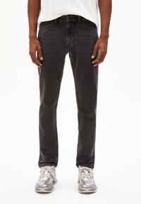 Jeans en denim noir avec une coupe slim, design à cinq poches et décoloration subtile, associés à des baskets grises avec des accents blancs et des lacets.