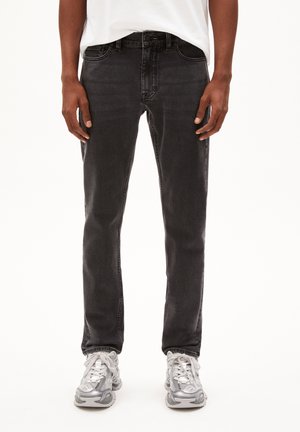 Schwarze Denim-Jeans mit schmaler Passform, Fünf-Taschen-Design und subtiler Ausbleichung, kombiniert mit grauen Sneakers mit weißen Akzenten und Schnürsenkeln.