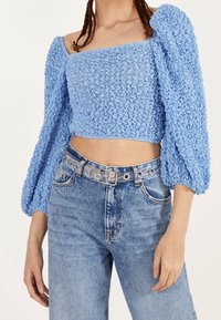 Světle modrý zkrácený top s texturovanou tkaninou, čtvercovým výstřihem a nabíranými rukávy. V snoubení s vysoce pasovými vybledlými džínami a průhledným opaskem.