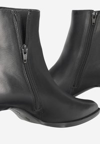 Bottes de cheville en cuir noir avec deux zips latéraux, design à bout pointu et talon bas. Texture lisse avec des détails de couture subtils.