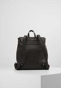 Mochila de cuero negro con un diseño estructurado, dobles asas superiores, correas ajustables y acentos de herrajes dorados. Textura suave con un diseño minimalista.