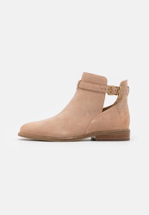 Bottine en daim beige clair avec bout arrondi, découpe latérale et sangle décorative à la cheville ornée d'une boucle dorée et talon bas.