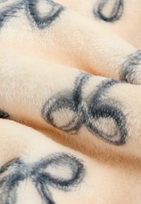 Weiche, pfirsichfarbene Decke mit subtilen schwarzen Unendlichkeitsschleifenmustern. Die Textur ist plüschig mit einem glatten, samtigen Finish.