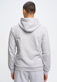 Sudadera gris con capucha, con una textura suave, puños y dobladillo acanalados, y un corte relajado, mostrada desde la parte de atrás.