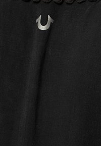 Mustat kankaat, joissa on ylälaitaan ommeltu reuna, teksturoitu kuvio ja hopeinen hevosenkenkälogo esillä selvästi.