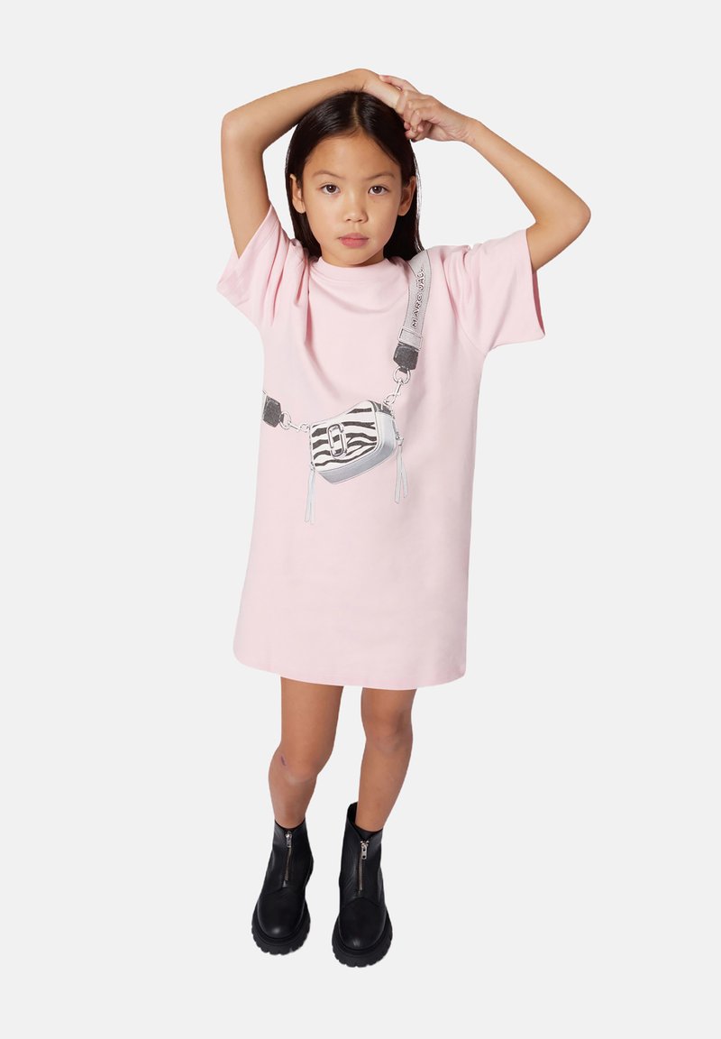 Robe t-shirt oversize rose avec un graphique d'un sac à rayures zèbre. Associée à des bottes à zip noires chevilles et un design minimaliste.