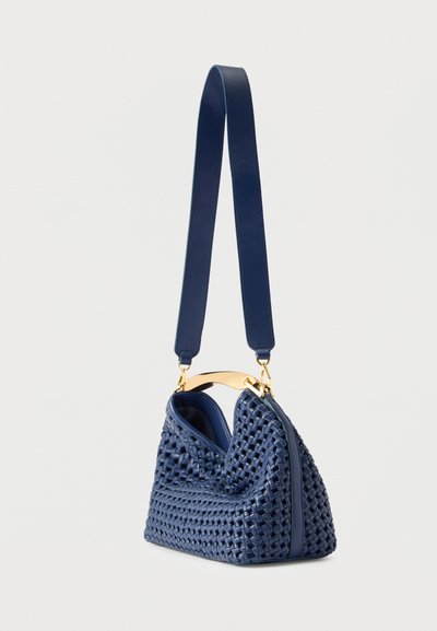 Τσάντα ώμου από ύφαντο δέρμα σε ναυτικό μπλε, με φαρδιά ιμάντα ώμου και χρυσή μεταλλική λαβή, τοποθετημένη σε απλό λευκό φόντο.