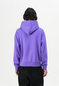 Lila Kapuzenpullover mit lockerer Passform, gerippten cuffs und Saum. Besitzt eine weiche Textur und keine sichtbaren Muster oder Logos. Schwarze Hose abgebildet.