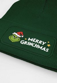 Green knit beanie featuring a woven patch with a Grinch graphic and the text "MERRY GRINCHMAS" in white, accented by stars.