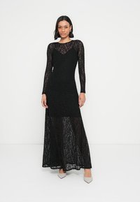 Črna maxi obleka iz čipke z dolgimi rokavi, s prilegajočim se zgornjim delom in prosojnim spodnjim delom. Opremljena z okroglim izrezom in subtilno teksturo.