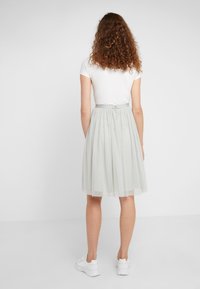 Gonna in tulle grigio chiaro con motivo a pois, vita arricciata e chiusura con cerniera. Abbinata a una maglietta bianca a maniche corte e sneakers bianche.