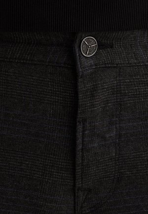 I pantaloni a scacchi neri e grigi presentano una texture liscia, un design elegante e un bottone metallico lucido in vita con un logo.
