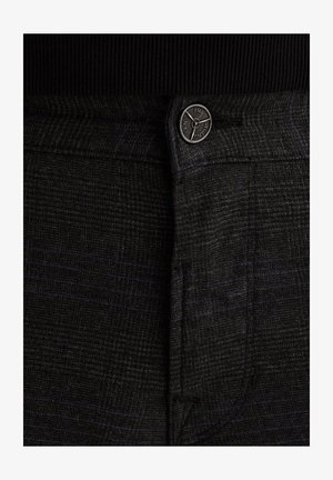 Zwart en grijs geruite broeken hebben een gladde structuur, een elegante uitstraling en een gepolijste metalen knop aan de taille met een logo.