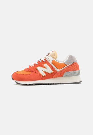 Orangener und grauer New Balance Sneaker mit Wildleder- und Mesh-Einsätzen, weißen Schnürsenkeln sowie einer weißen und grauen Sohle auf schlichtem Hintergrund.