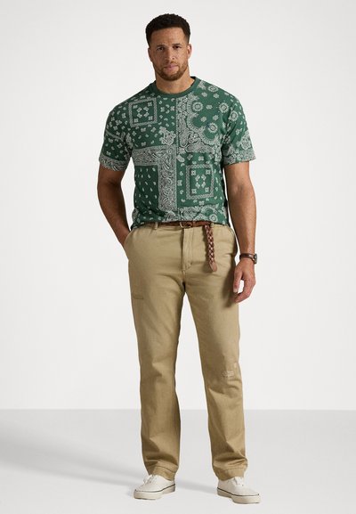 Grønn bandana-mønstrete kortermet skjorte med hvite detaljer, paret med beige straight-leg bukser og hvite joggesko.