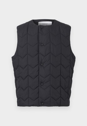 Melna bez piedurknēm dūnu veste ar sprādžu aizdari un vaļveida šūšanas rakstu, ar Maison Kitsuné etiķeti apkakles iekšpusē.