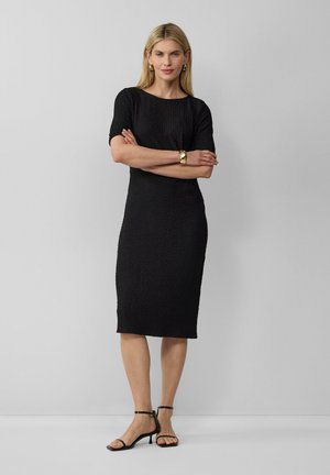 Robe noire midi avec un motif texturé, manches courtes, col rond et une silhouette cintrée, associée à des talons noirs à lanières.