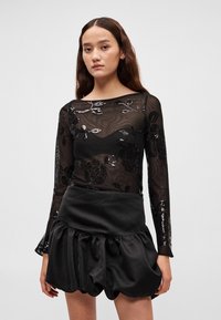 Top preto transparente com bordado floral e lantejoulas, combinado com uma saia bufante de cetim preta com cintura alta e design franzido.
